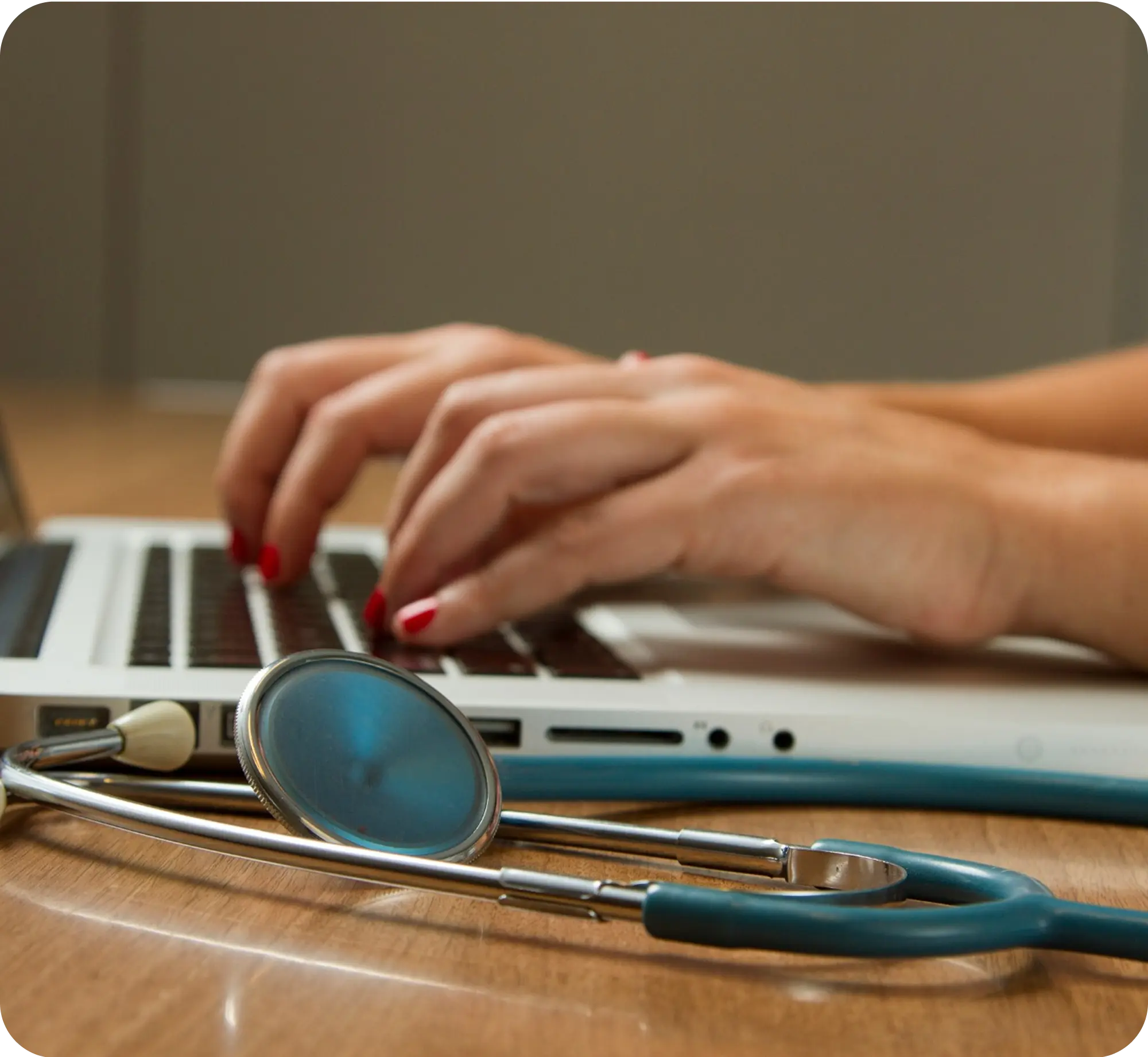 Hands typing on laptop with stethoscope resting on desk nearby