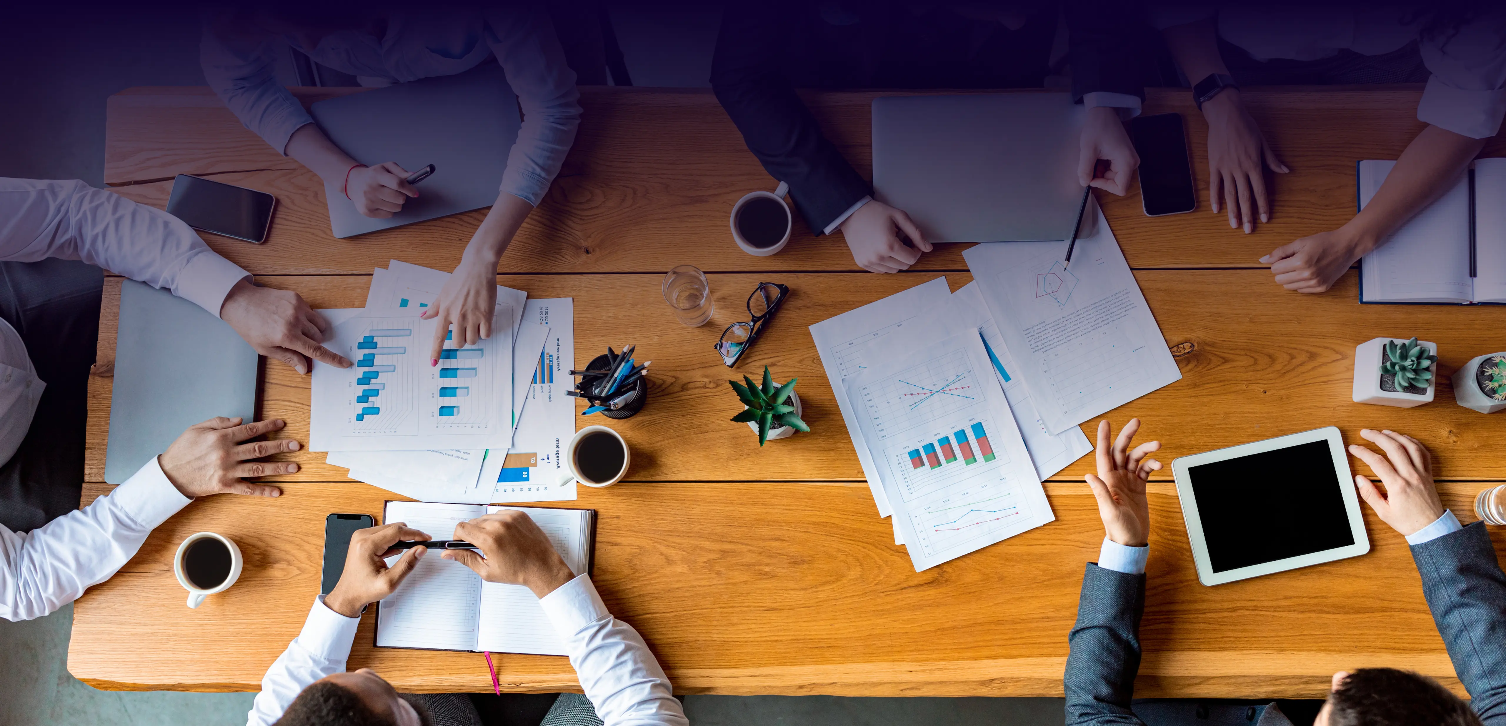 Overhead view of business meeting with documents and laptops on table.