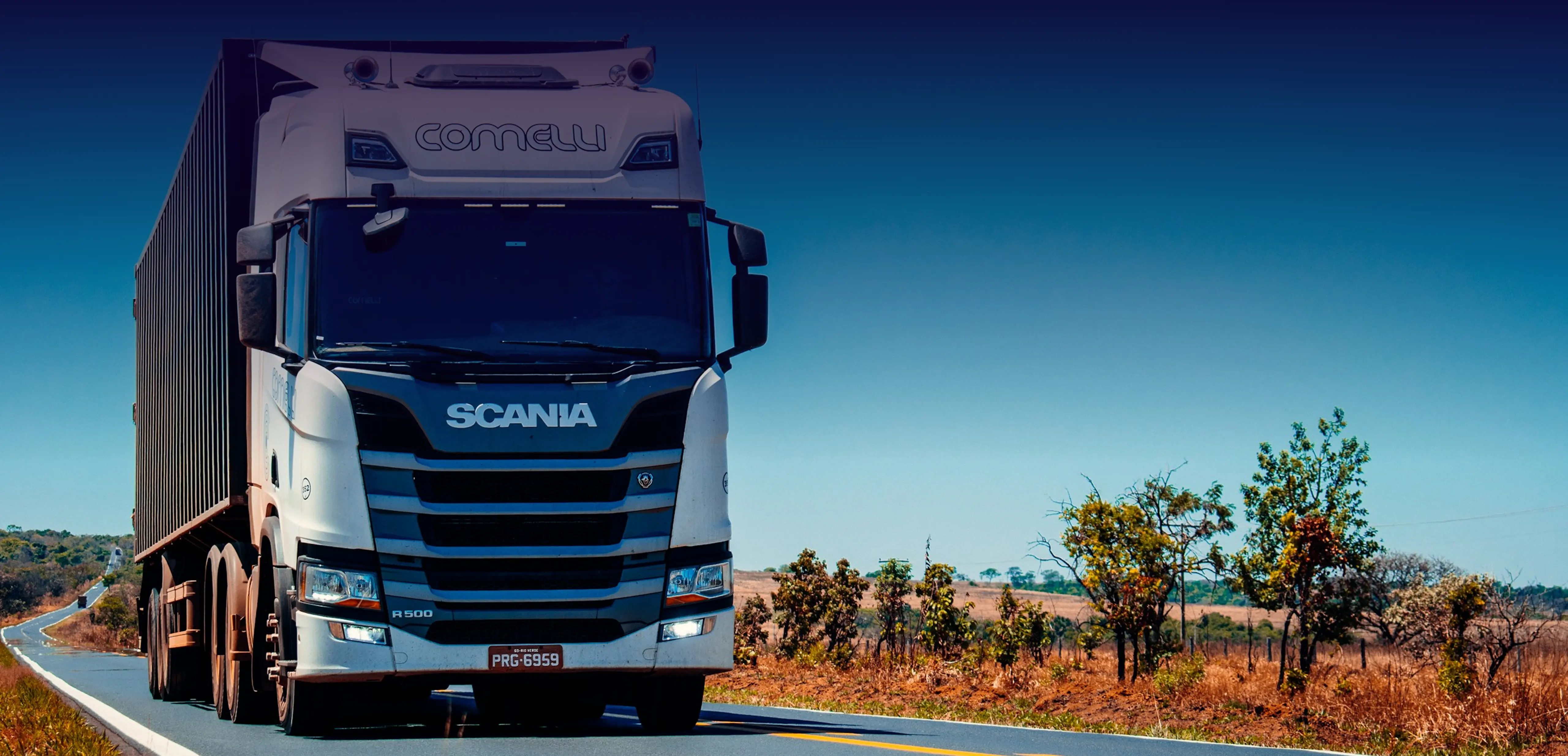 White Scania R500 truck driving on rural highway under blue sky.